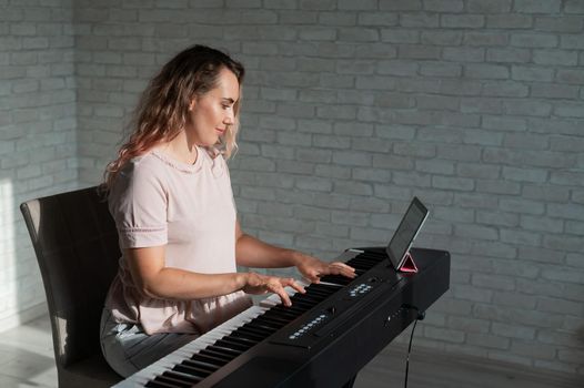 Caucasian woman remotely teaches electric piano playing via video communication on a digital tablet.