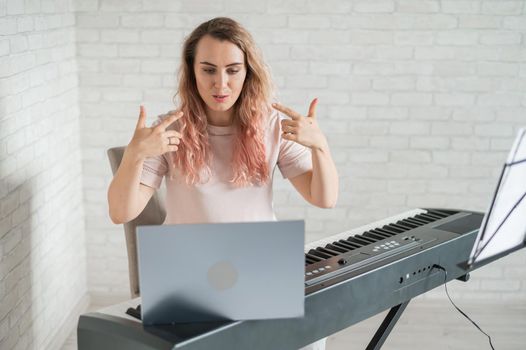 A friendly woman plays the electronic piano and conducts a video blog on her laptop. Stay home. Musical instrument teacher. Distance learning music quarantined