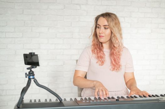 A woman plays the electronic piano and conducts a video blog on a smartphone. A girl takes video from a phone on a tripod. Female music teacher works remotely