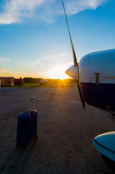 A blue suitcase and a parked small private jet. Quadruple plane with a propeller for an air taxi in the sunset. Self travel concept. plane for VIP persons