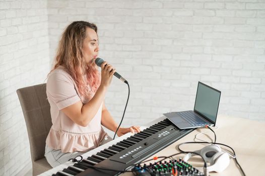 A woman records a vocal lesson using a laptop and accompanying on a keyboard while at home. The teacher sings a song into the microphone and plays the electronic piano. A blogger is recording a video