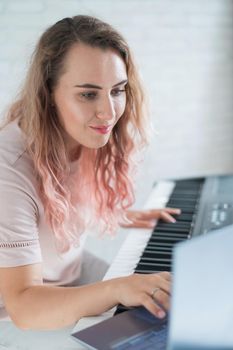 A friendly woman plays the electronic piano and conducts a video blog on her laptop. Stay home. Musical instrument teacher. Distance learning music quarantined