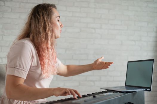 A friendly woman plays the electronic piano and conducts a video blog on her laptop. Stay home. Musical instrument teacher. Distance learning music quarantined