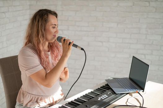 A woman sings into a microphone and shoots a video blog on a laptop.