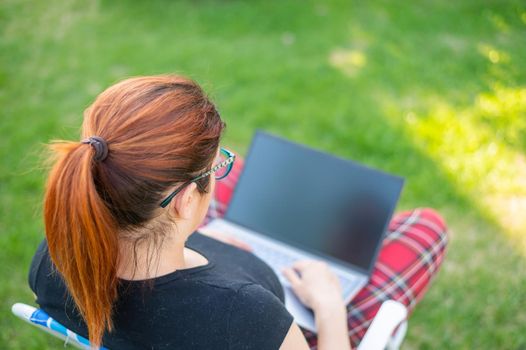 woman sits in a park and types on the computer while shopping online. The girl maintains a social distance and works outdoors on a laptop. The student is studying remotely