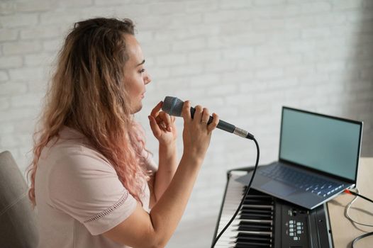 A woman sings into a microphone and shoots a video blog on a laptop.