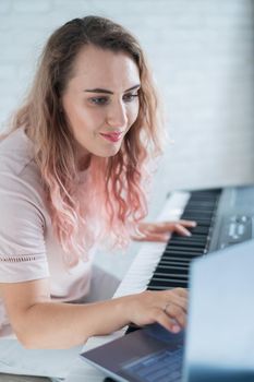 A friendly woman plays the electronic piano and conducts a video blog on her laptop. Stay home. Musical instrument teacher. Distance learning music quarantined