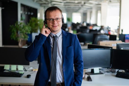 A friendly man from a call center answers a customer with a hands-free headset. Male helpdesk operator talking on the phone. Manager in open space office