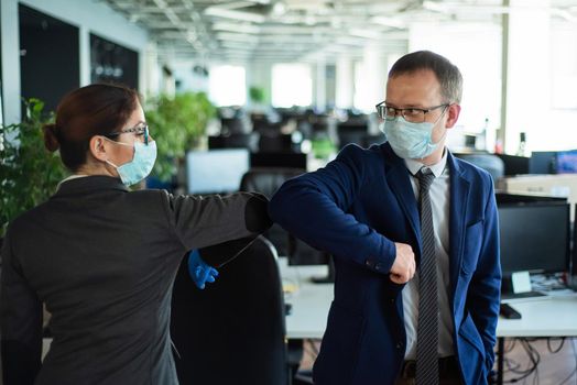 Office workers shake hands when meeting and greet bumping elbows. A new way to greet the obstructing spread of coronavirus. Man and woman in protective masks maintain a social distance at work