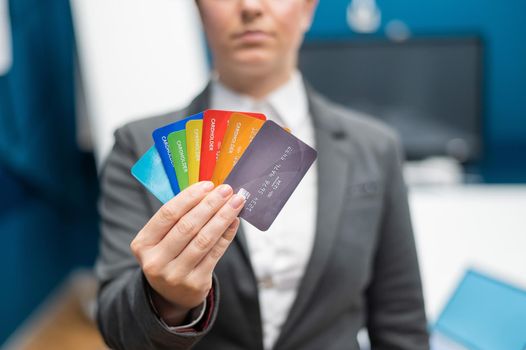 Unrecognizable woman dressed in a suit holds multi-colored plastic credit cards. A faceless bank employee offers a loan. Shopping concept. Close-up of female hands with debit cards