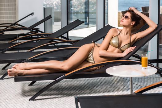 Body care. Woman with perfect body in bikini lying on the deckchair by swimming pool at resort spa hotel.