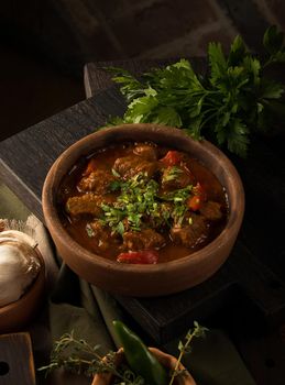 A close up shot of a meat stew and herbs in the background