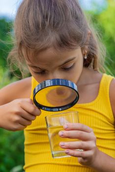 The child examines a glass of water with a magnifying glass. Selective focus. Kid.