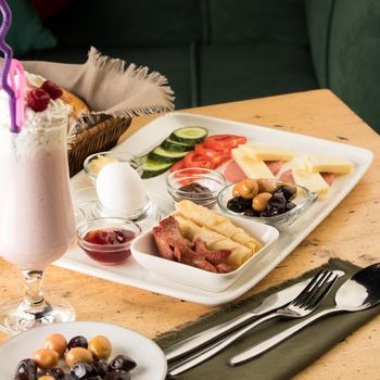 A closeup shot of a breakfast white plate and a cup of smoothie on a wooden table