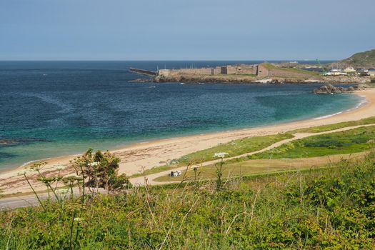 View across bay and sandy beach to Fort Grosnez and Braye Harbour from Fort Tourgis under blue sky, Alderney, Channel Islands