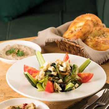 A close up shot of a salad and appetizers near basket of breads