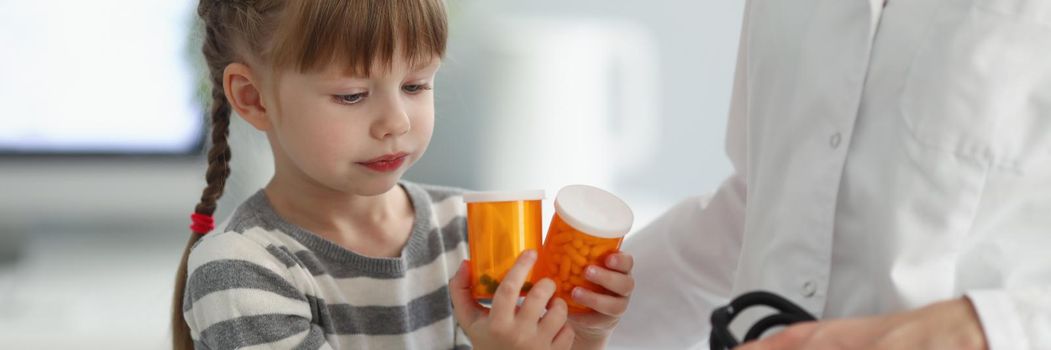 Portrait of child playing with bottles full of medication while on doctors appointment. Female doctor hold stethoscope for examining. Pediatrician concept