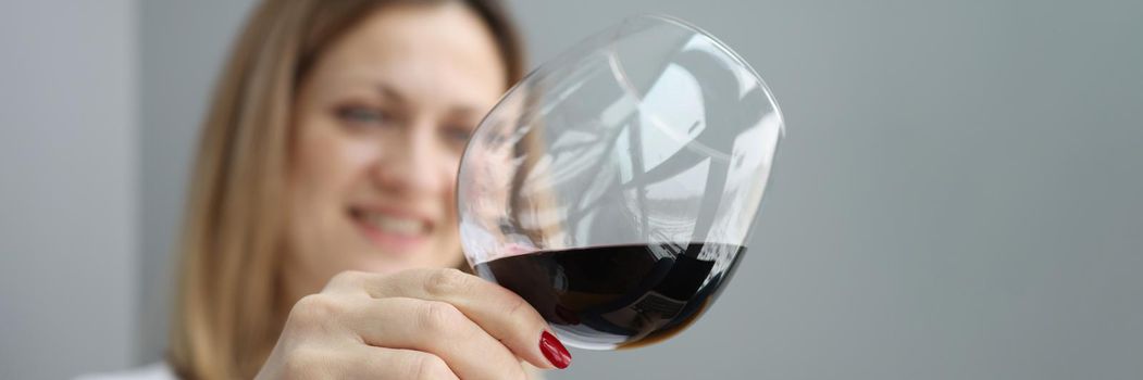 Close-up of young pretty woman holding glass of exquisite red wine and slants liquid inside. Enjoy evening alone and taste of drink. Relax, weekend concept
