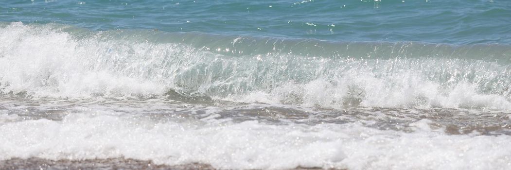 Close-up of blue sea waves with white foam on marine sand beach. Time to rest and summer holidays concept. Travelling and vacation, seascape background