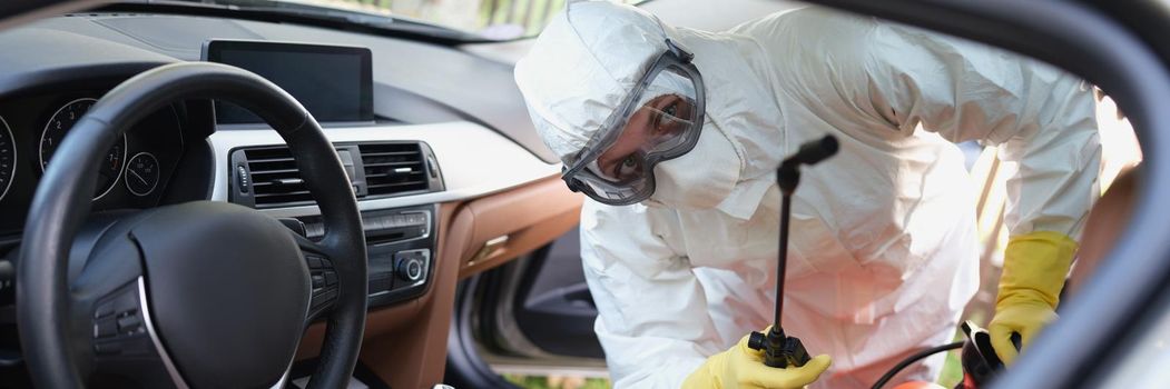 Close-up of person in protective costume clean surfaces in car with disinfectant spray. Help kill coronavirus in car after going out. Stop virus concept