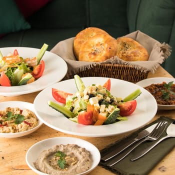 A dining table full of delicious salad on a white plate next to basket of bread