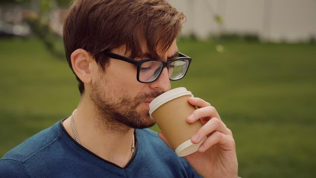 Young sad man. Unhappy alone man working outdoor. Closeup face of handsome guy with sad eyes, on the nature drink coffee.