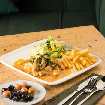 A closeup of a meal with chicken, french fries, salad and olives on a table