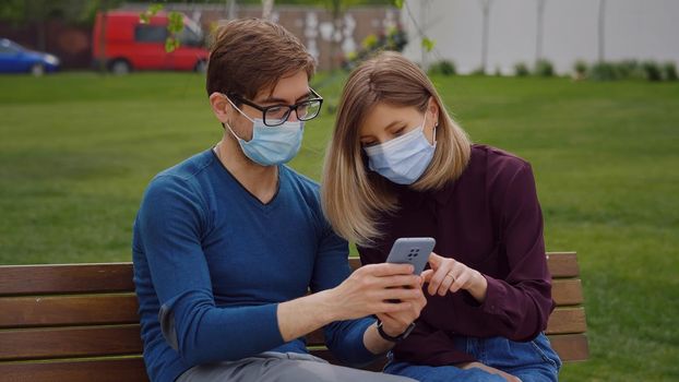 Two cute people look closely on phone and find out from news Couple sitting on bench, green background.