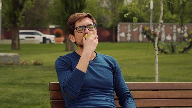 Handsome Man Eating Heathy food. Apple as Healthy Snack. Enjoying an fruit. Male Portrait have snack in park.