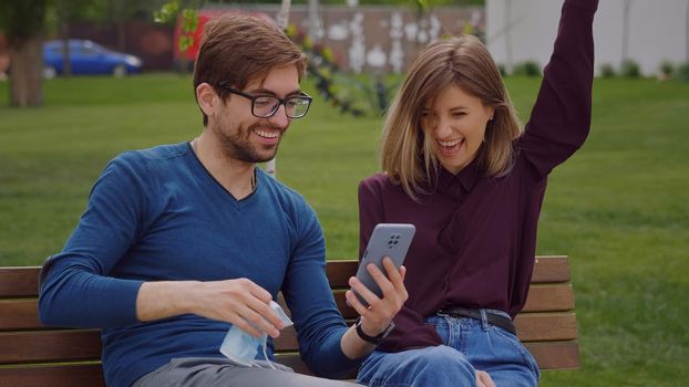 Happy news concept. Two friends find out end of covid-19 news Coronavirus pandemic is over. Take off their masks exclaimed joy Couple sitting on bench outdoor