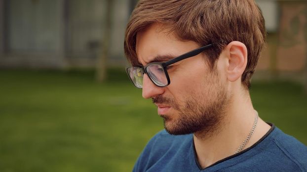 Man works on his laptop while sat on a bench outdoors. Focused facial expressions. Concentration facial Portrait. Working responsibly. Handsome young man write a serious mail.