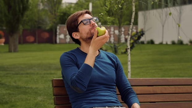 Young man Eating a apple as snack. Enjoying an fruit. Male Portrait have snack in park.