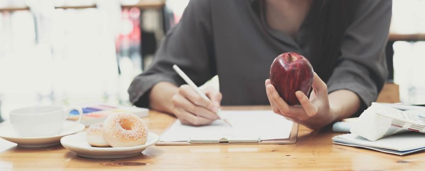 Attractive young asian female graphic designer eating an apple and sketching designing her design on paper at her office desk..