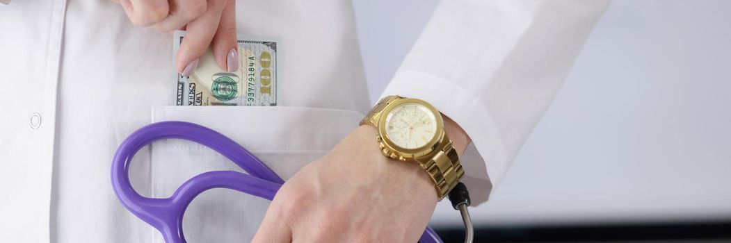 Close-up of woman doctor carry stethoscope tool and show piece of banknote in pocket. Pay to get qualified advice. Corruption in medicine, health concept
