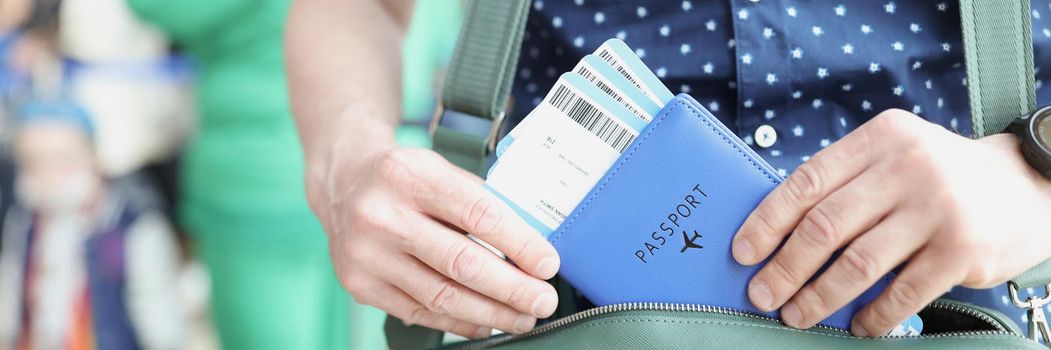 Close-up of male hands holding passport and boarding pass. Man putting documents in bag. Boarding plane and departure lounge in airport. Travelling abroad concept