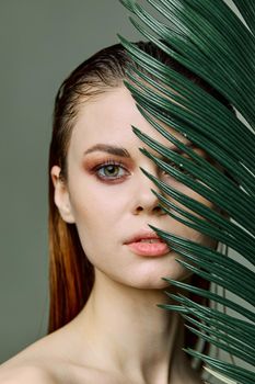 a close beauty portrait of a beautiful woman standing holding a tropical palm leaf in her hand, bringing it to her face, looking into the camera. Vertical photo without retouching of problem skin. High quality photo