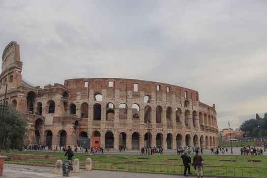 ROME, ITALY - February 05, 2022: Panoramic view around the Colosseum in city of Rome, Italy. Cold and gray sky in the background. Macro photography of the green parks with the old buildings.