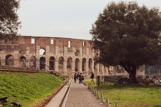 ROME, ITALY - February 05, 2022: Panoramic view around the Colosseum in city of Rome, Italy. Cold and gray sky in the background. Macro photography of the green parks with the old buildings.