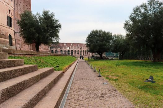 ROME, ITALY - February 05, 2022: Panoramic view around the Colosseum in city of Rome, Italy. Cold and gray sky in the background. Macro photography of the green parks with the old buildings.