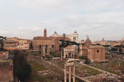 ROME, ITALY - February 05, 2022: Panoramic view around the Colosseum in city of Rome, Italy. Cold and gray sky in the background. Macro photography of the green parks with the old buildings.