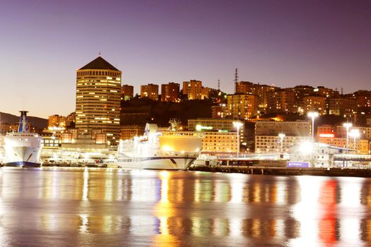 Genova, Italy - February 22, 2022: Evening view of Genoa (Genova) port, Italy with port cranes and industrial zone. Genoa, Italy. Lanterna lights by night. City illuminated behind the sea.