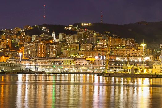 Genova, Italy - February 22, 2022: Evening view of Genoa (Genova) port, Italy with port cranes and industrial zone. Genoa, Italy. Lanterna lights by night. City illuminated behind the sea.