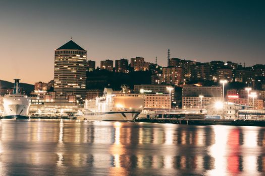 Genova, Italy - February 22, 2022: Evening view of Genoa (Genova) port, Italy with port cranes and industrial zone. Genoa, Italy. Lanterna lights by night. City illuminated behind the sea.