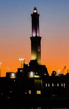 Genova, Italy - February 22, 2022: Evening view of Genoa (Genova) port, Italy with port cranes and industrial zone. Genoa, Italy. Lanterna lights by night. City illuminated behind the sea.