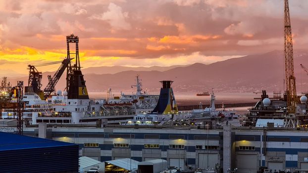 Genova, Italy - February 22, 2022: Evening view of Genoa (Genova) port, Italy with port cranes and industrial zone. Genoa, Italy. Lanterna lights by night. City illuminated behind the sea.