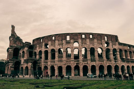 ROME, ITALY - February 05, 2022: Panoramic view around the Colosseum in city of Rome, Italy. Cold and gray sky in the background. Macro photography of the green parks with the old buildings.