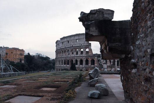 ROME, ITALY - February 05, 2022: Panoramic view around the Colosseum in city of Rome, Italy. Cold and gray sky in the background. Macro photography of the green parks with the old buildings.