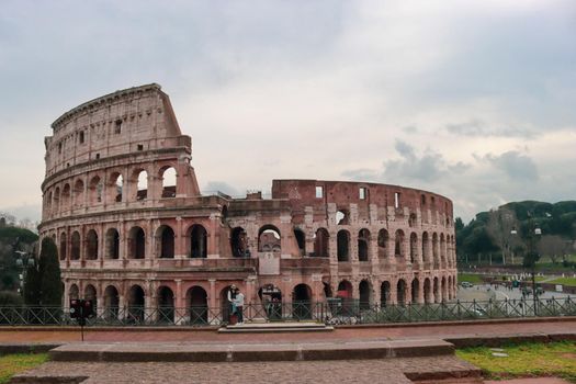 ROME, ITALY - February 05, 2022: Panoramic view around the Colosseum in city of Rome, Italy. Cold and gray sky in the background. Macro photography of the green parks with the old buildings.