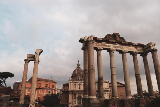 ROME, ITALY - February 05, 2022: Panoramic view around the Colosseum in city of Rome, Italy. Cold and gray sky in the background. Macro photography of the green parks with the old buildings.