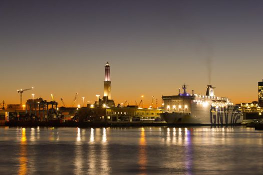 Genova, Italy - February 22, 2022: Evening view of Genoa (Genova) port, Italy with port cranes and industrial zone. Genoa, Italy. Lanterna lights by night. City illuminated behind the sea.